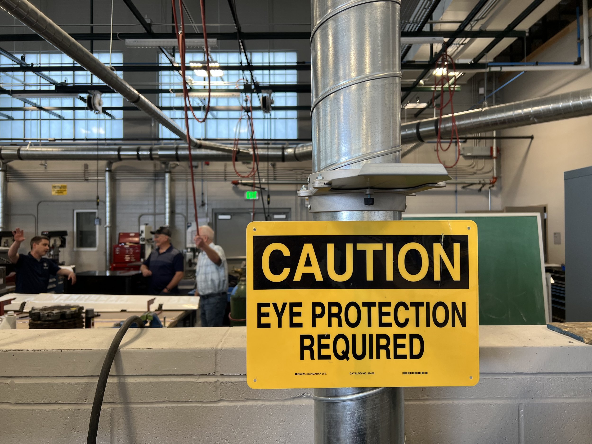 Safety sign in the foreground, instructors and. visitor in the background